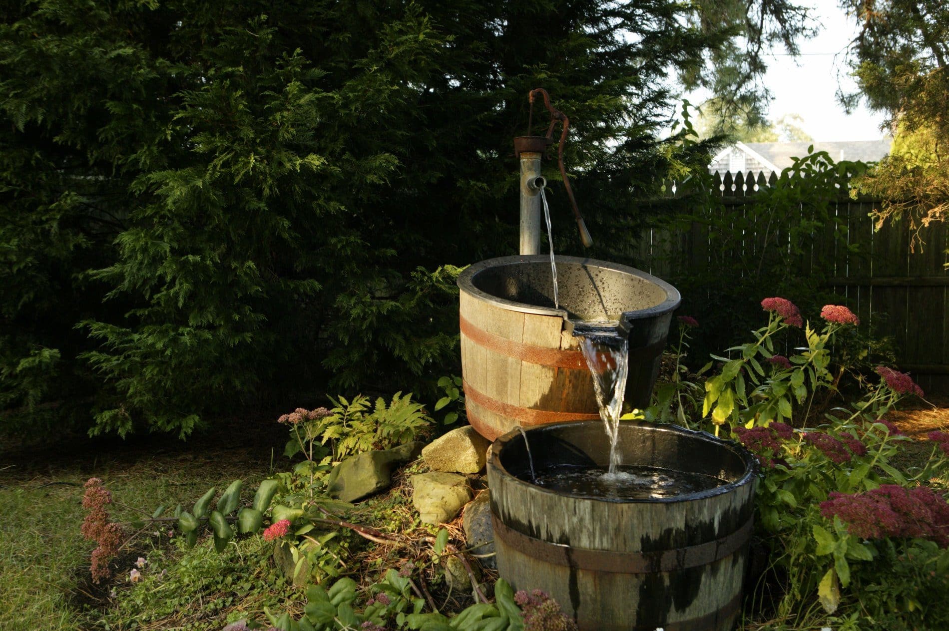 Outside lawn with wooden fence, lush trees and rain barrel water fountain feature